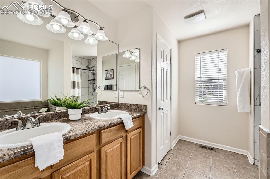 Image 17 of 39: Bathroom with double vanity, light tile patterned floors, and a stall showe