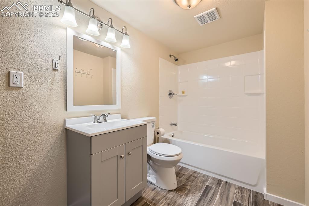 Image 34 of 39: Full bath with a textured wall, vanity, wood finish floors, and bathtub / s