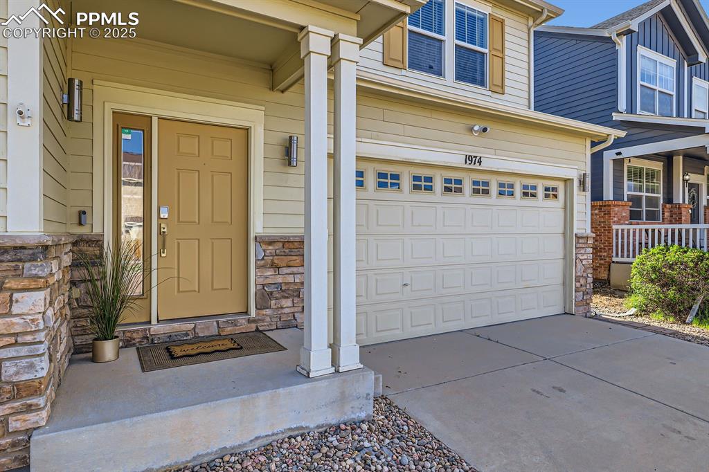 Image 4 of 39: Entrance to property with stone siding, concrete driveway, a porch, and a g