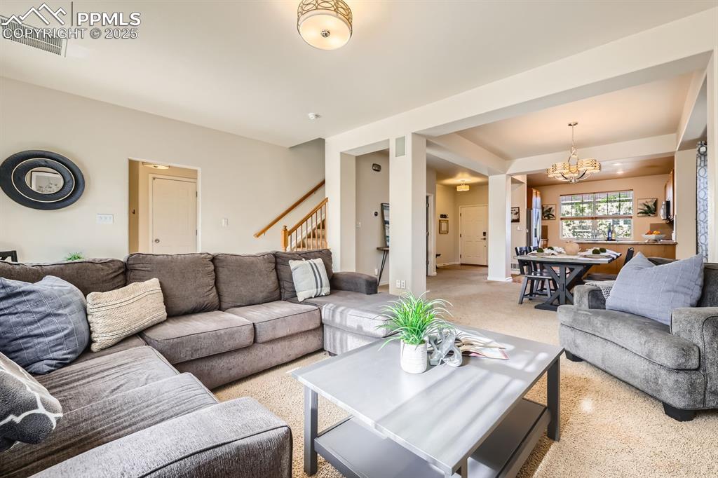 Image 7 of 39: Living room with carpet, a chandelier, and stairs
