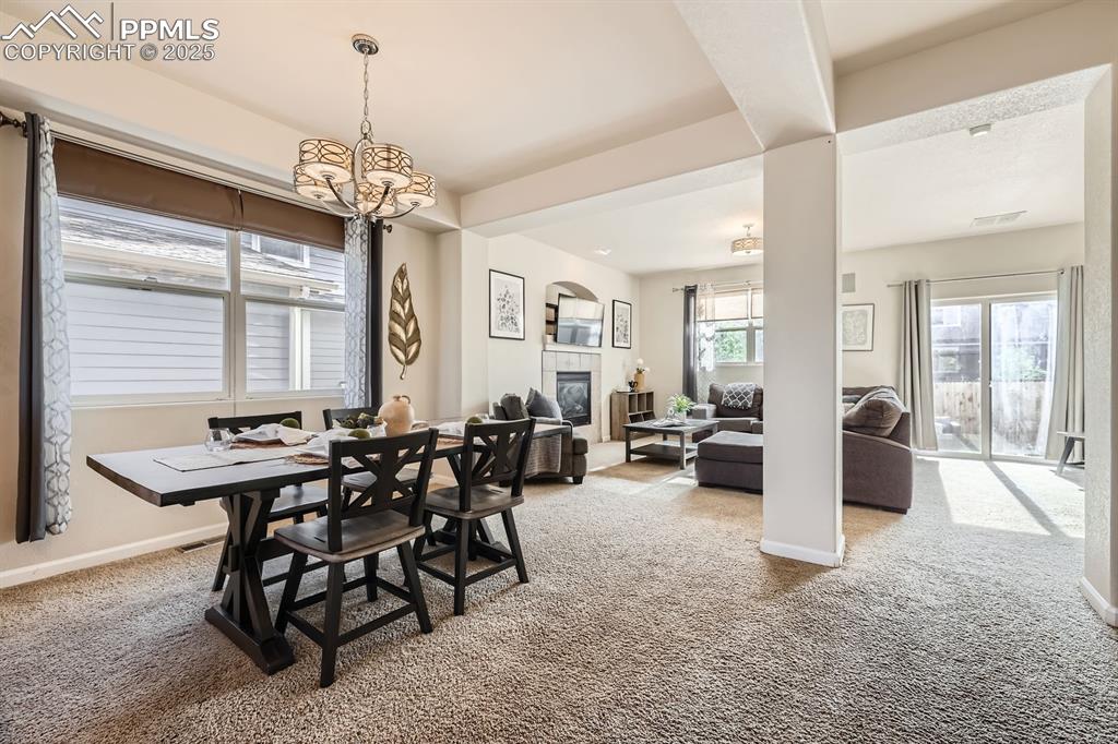 Image 9 of 39: Dining space featuring light carpet, a fireplace, and a chandelier