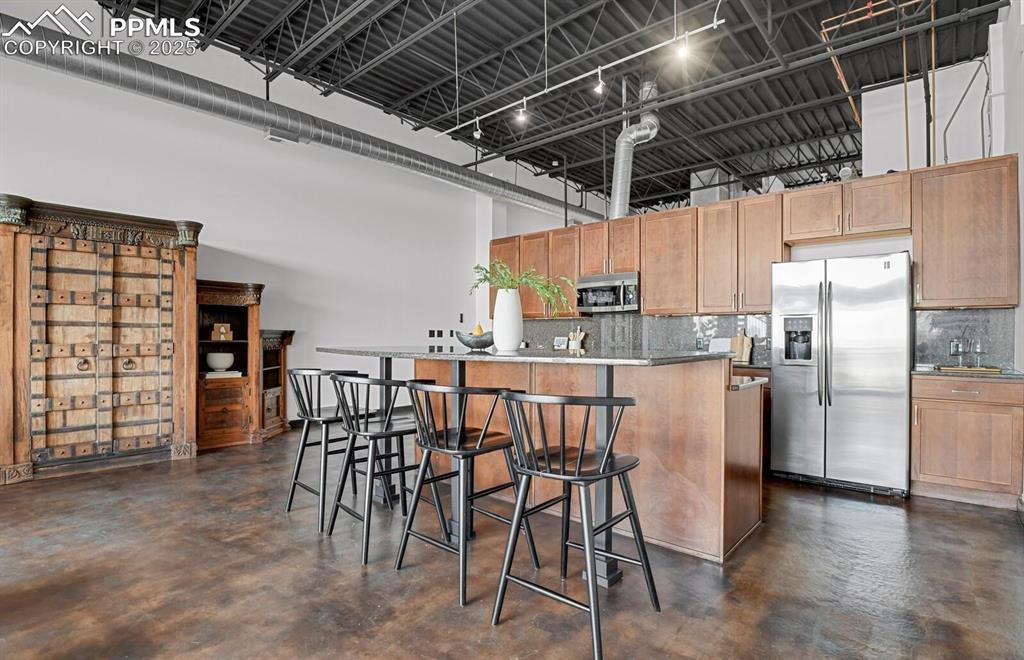 Image 16 of 45: Kitchen featuring backsplash, concrete flooring, a high ceiling, and applia