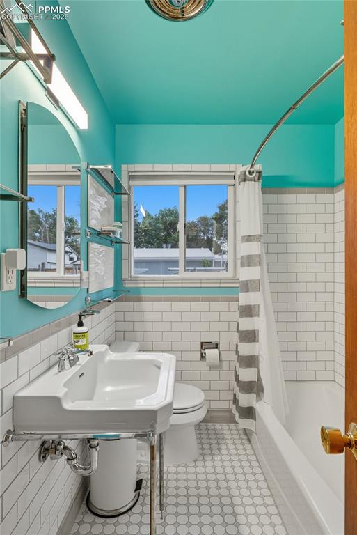 Image 18 of 39: Bathroom featuring shower / bath combo with shower curtain, tile walls, and