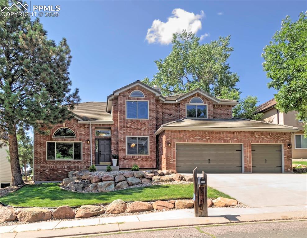 Caption: Traditional-style house featuring brick siding, concrete driveway, a front lawn, and a garage