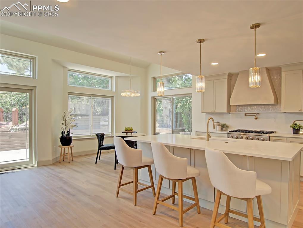 Image 14 of 50: Kitchen featuring wall chimney range hood, light countertops, light wood-ty