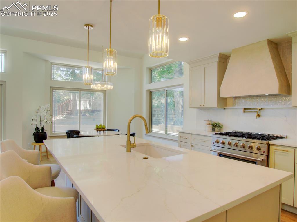Image 20 of 50: Kitchen featuring a chandelier, high end stove, custom range hood, an islan