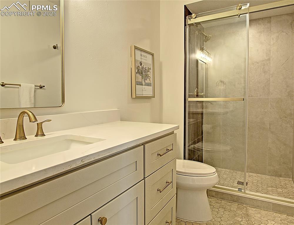 Image 27 of 50: Main Level Full bath featuring vanity, a shower stall, and tile patterned f