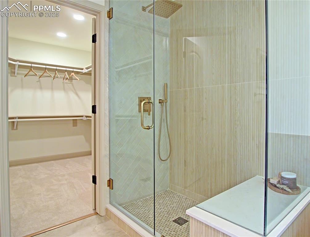 Image 34 of 50: Primary Bathroom with a shower stall, a walk in closet, tile patterned floo