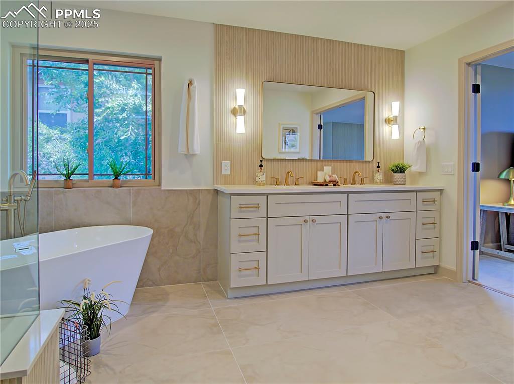 Image 36 of 50: Bathroom featuring double vanity, a freestanding tub, and tile walls