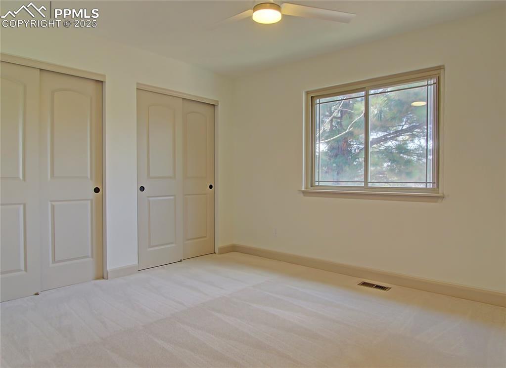 Image 38 of 50: bedroom featuring light carpet, multiple closets, and a ceiling fan