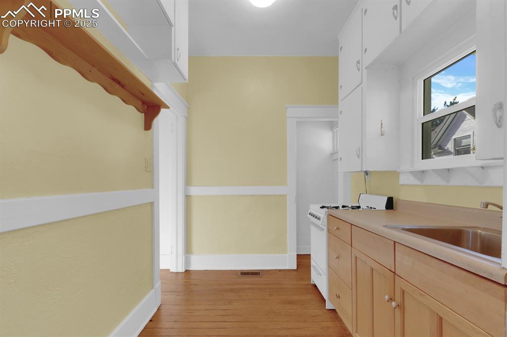 Image 19 of 28: Kitchen with white gas range, light brown cabinets, light wood-style floori