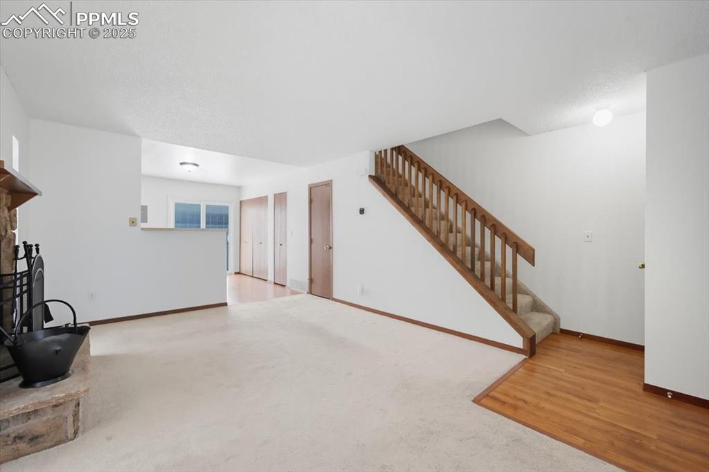 Image 18 of 34: Unfurnished living room with a fireplace, stairway, carpet, and wood finish