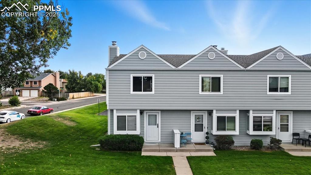 Image 24 of 34: Rear view of property featuring a lawn, a chimney, and roof with shingles