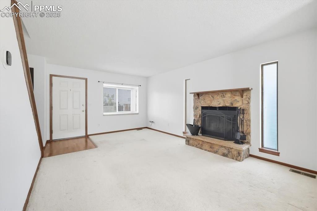 Image 4 of 34: Unfurnished living room with a stone fireplace and carpet