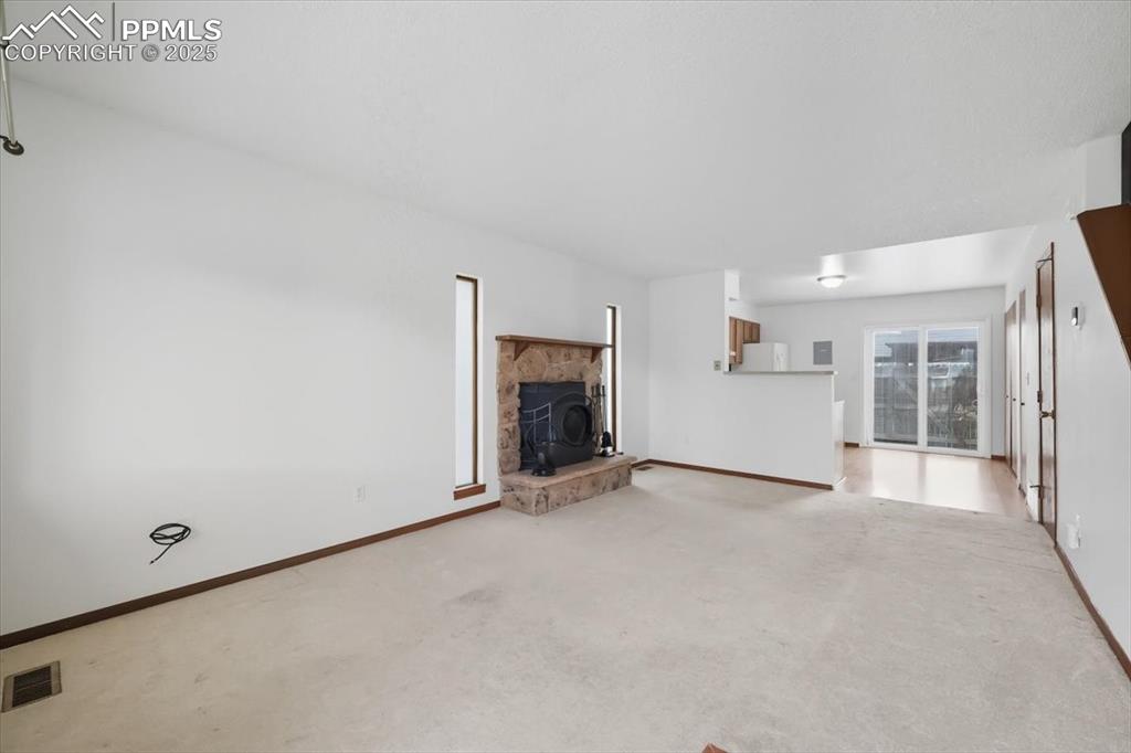 Image 5 of 34: Unfurnished living room with a wood stove and light colored carpet