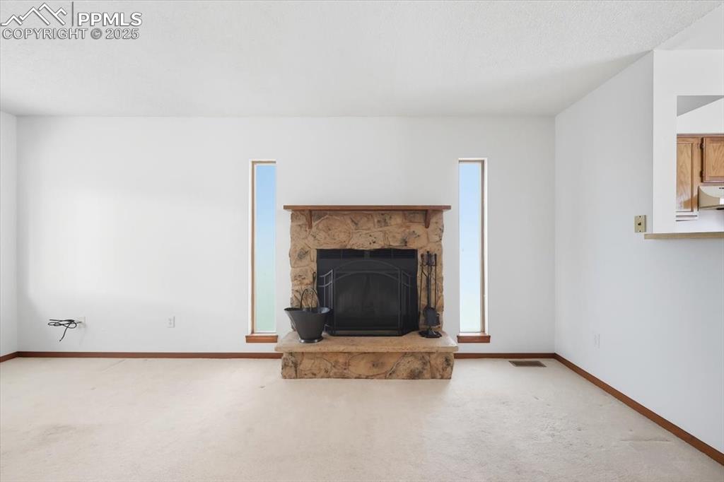 Image 9 of 34: Unfurnished living room with a stone fireplace and carpet floors