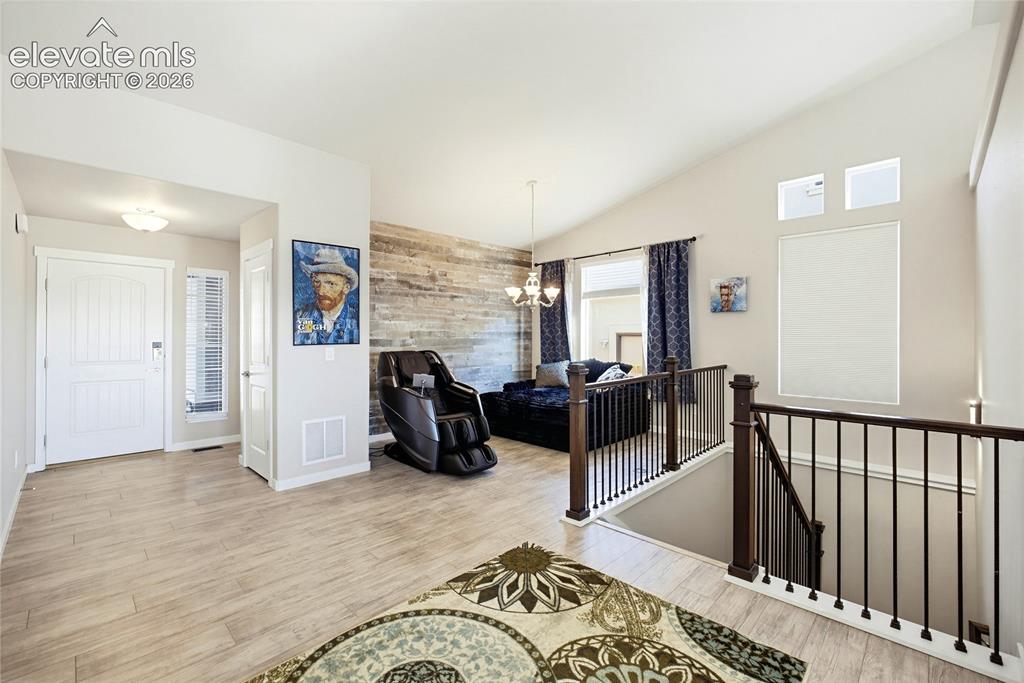 Image 14 of 50: Vaulted ceilings, wood-finish flooring, a wood-panel accent wall, and a sta