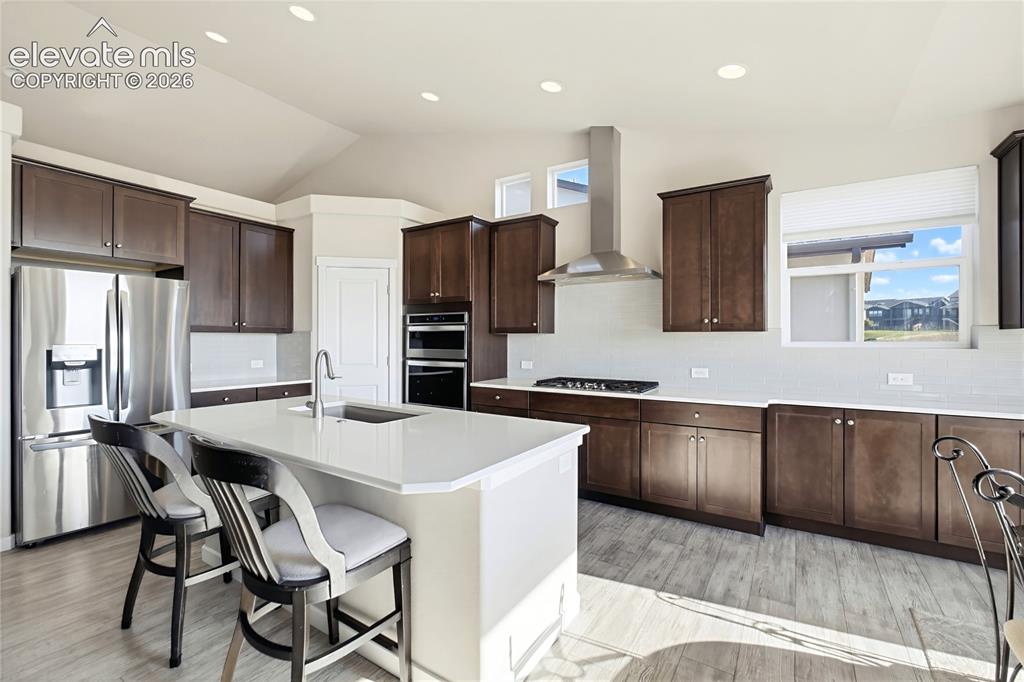 Image 29 of 50: Kitchen featuring dark wood cabinetry, quartz countertops, a central island