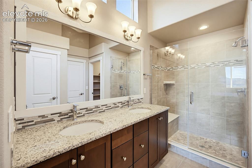 Image 37 of 50: Dual-sink vanity with stone-finish countertop, full-width mirror, glass-enc