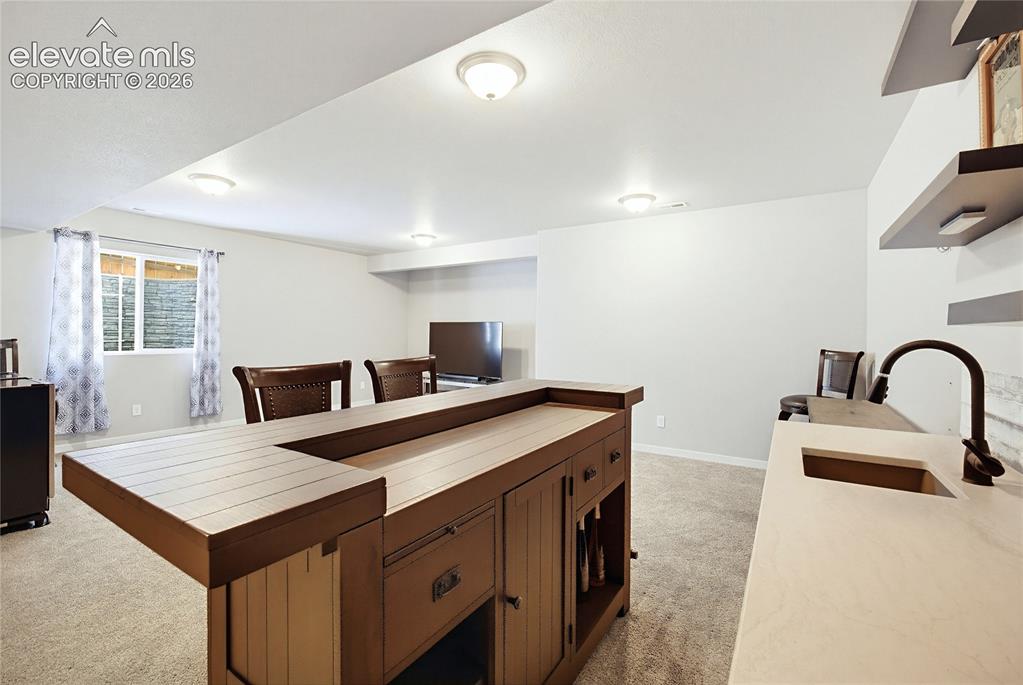 Image 44 of 50: Wet bar featuring a wooden counter, stone-finish countertop, integrated sin