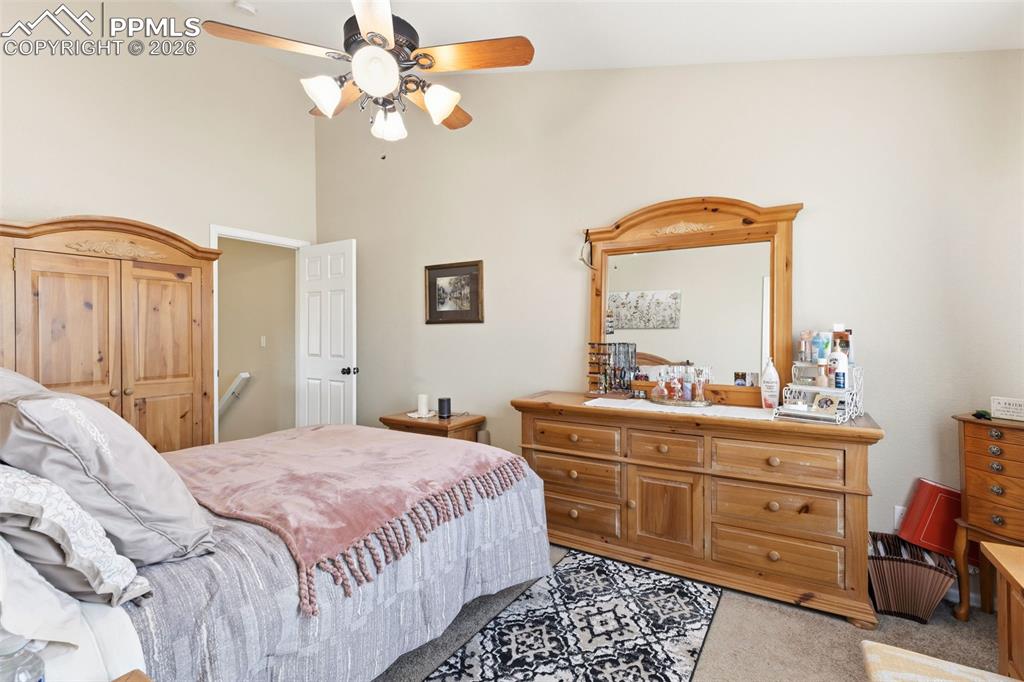 Image 17 of 26: Bedroom with light carpet, ceiling fan, and a high ceiling