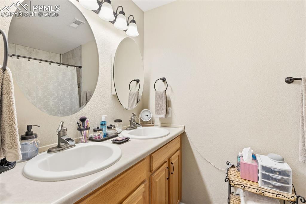 Image 19 of 26: Full bathroom with a textured wall, double vanity, and a shower with curtai