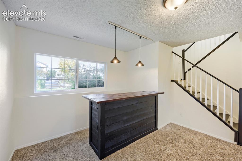 Image 18 of 35: Built-in bar with wood-finish countertop, track lighting with pendant fixtu