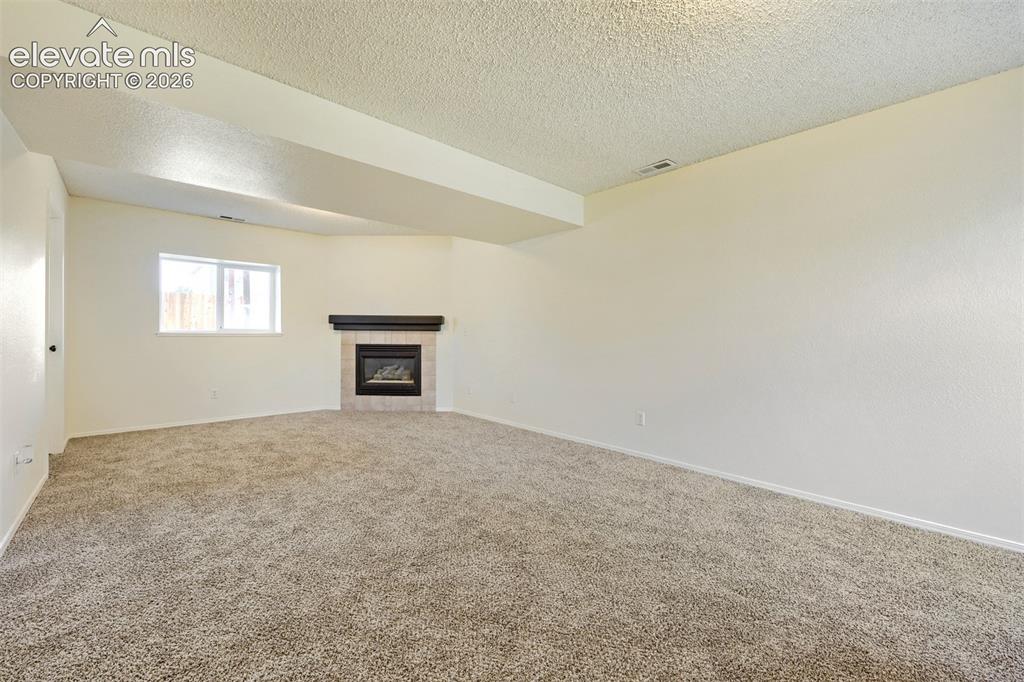 Image 19 of 35: Corner fireplace with a dark wood mantel and tile surround, accompanied by