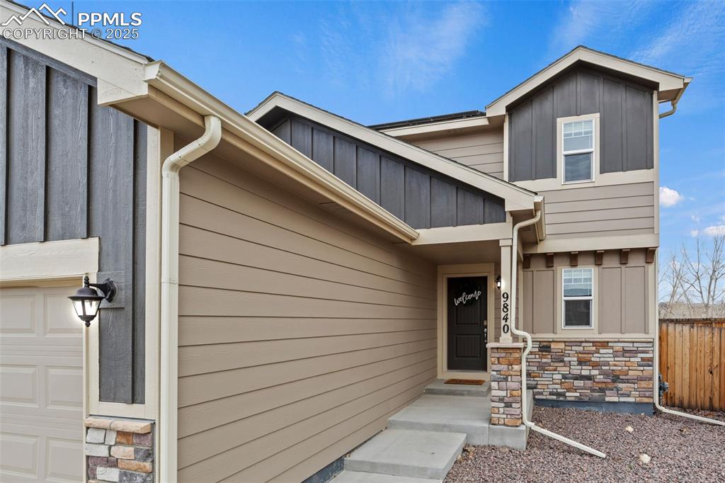 Image 4 of 48: Property entrance featuring fence, stone siding, board and batten siding, a