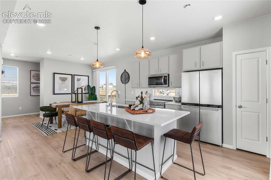 Image 11 of 31: Open-concept kitchen and dining area featuring light-toned wood-finish floo