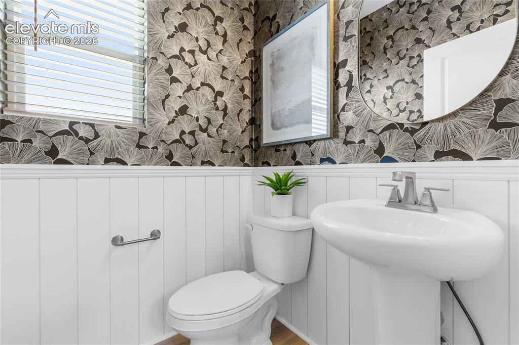 Image 21 of 31: Pedestal sink with a chrome faucet, white paneling, and patterned wallpaper