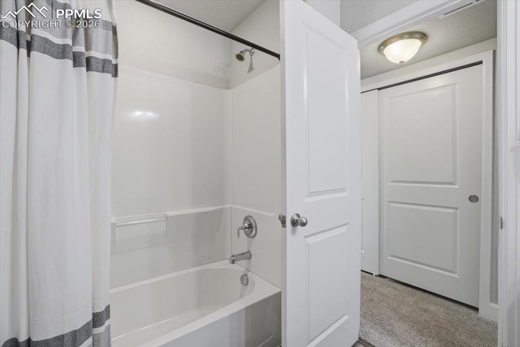 Image 36 of 47: The bathroom features a white bathtub with a shower, complemented by a whit