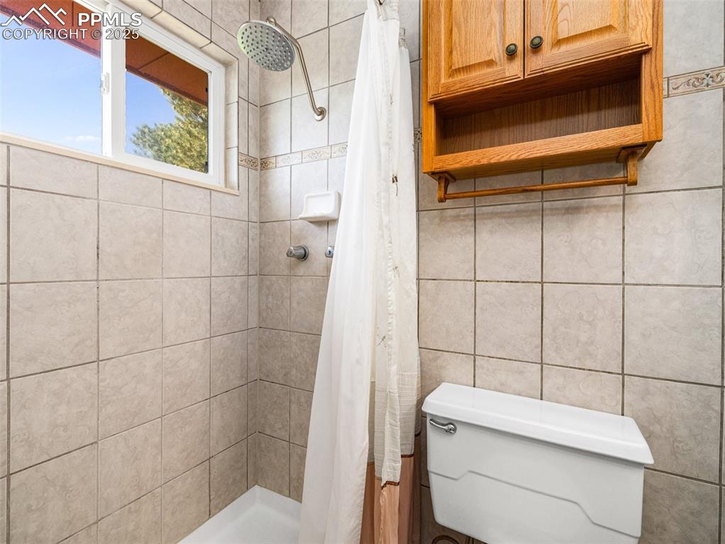 Image 25 of 38: Bathroom with a shower stall and tile walls