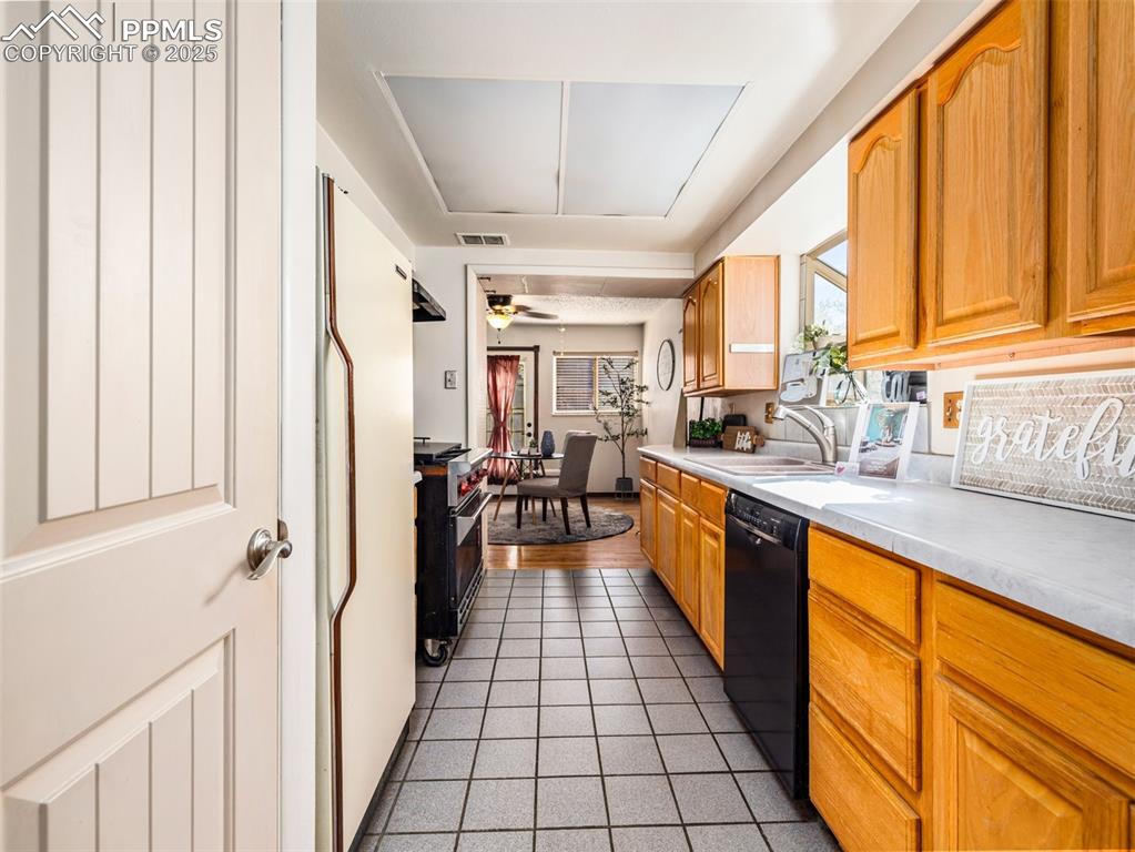 Image 6 of 38: Kitchen with dark tile patterned flooring, black dishwasher, freestanding r