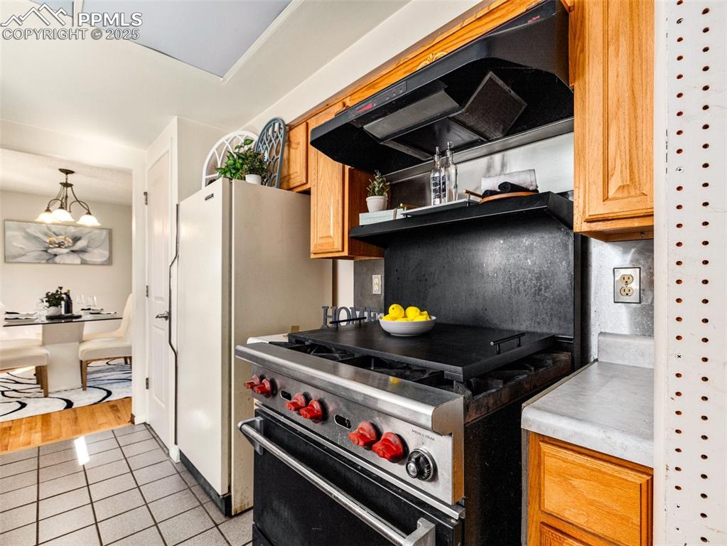 Image 7 of 38: Kitchen featuring designer stove, light countertops, exhaust hood, light ti