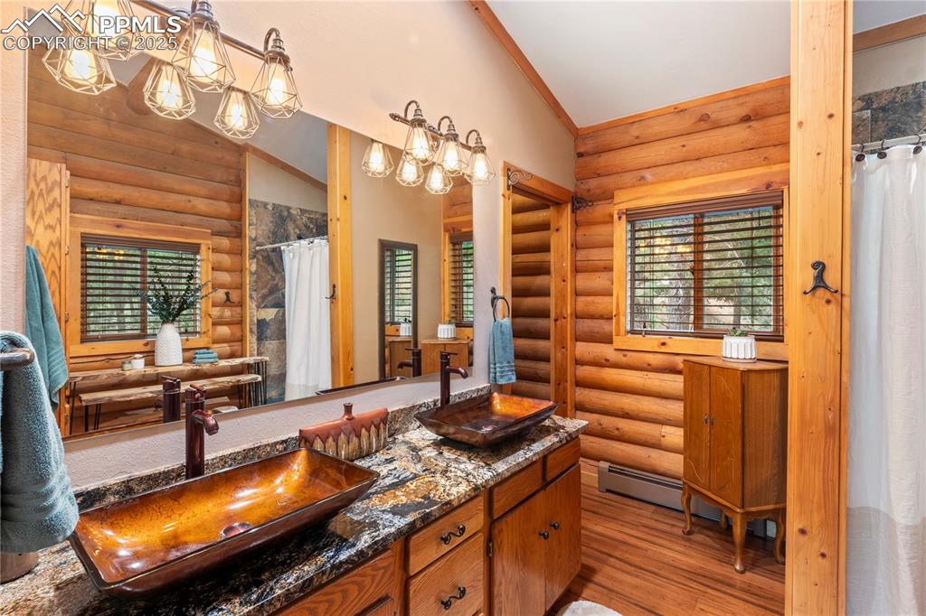 Image 24 of 46: Luxury primary bath w/granite counters, ceramic bowls, and warm wood floors
