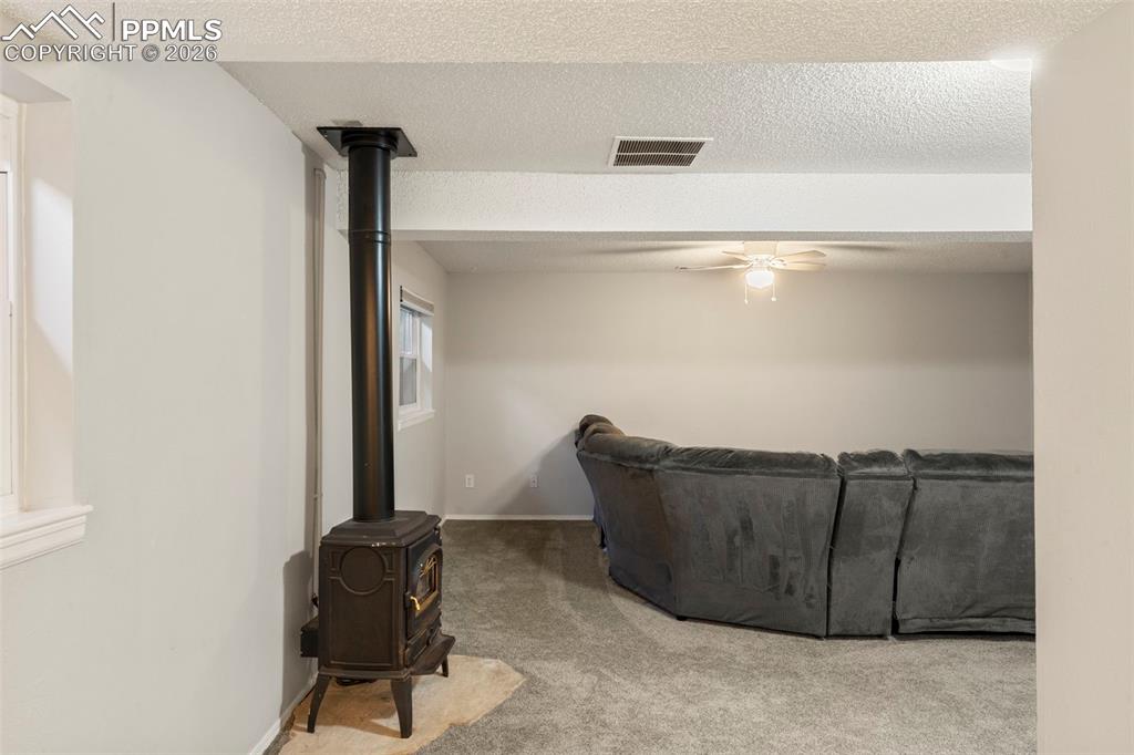 Image 20 of 29: Carpeted living room with a textured ceiling, a ceiling fan, and a wood sto