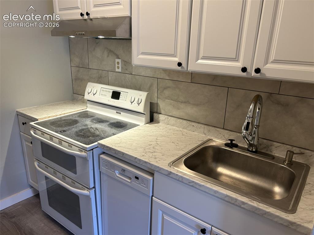 Image 35 of 45: White shaker-style cabinetry with black hardware, stainless steel sink with