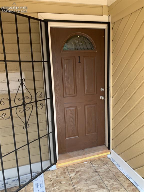 Image 7 of 45: Brown entry door with an arched glass insert, featuring an ornamental secur