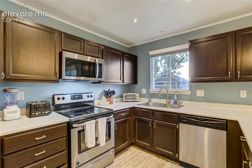 Image 11 of 40: Kitchen featuring dark wood-finish cabinetry, white countertops, and stainl