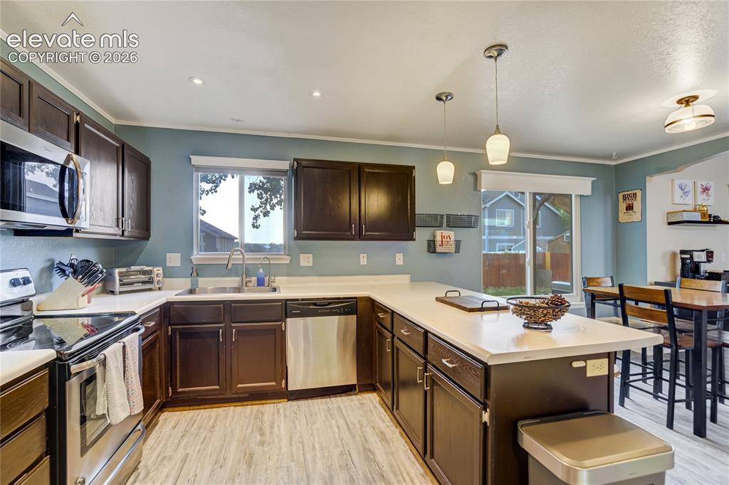 Image 12 of 40: Kitchen featuring dark wood cabinetry, light-toned countertops, stainless s