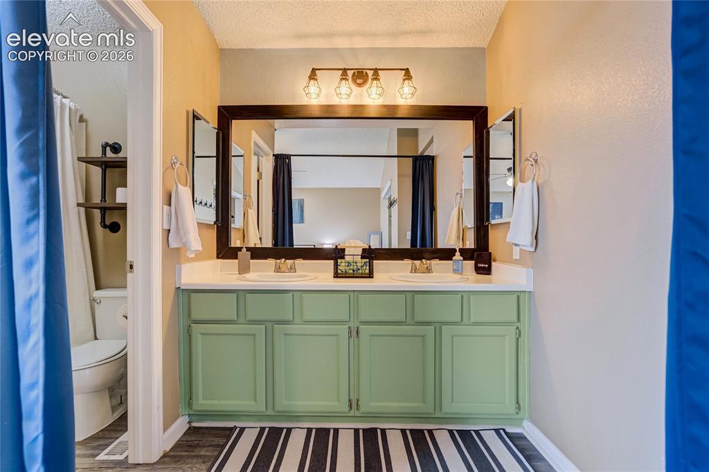 Image 20 of 40: Dual vanity with green cabinetry, white countertops, and brushed nickel fau