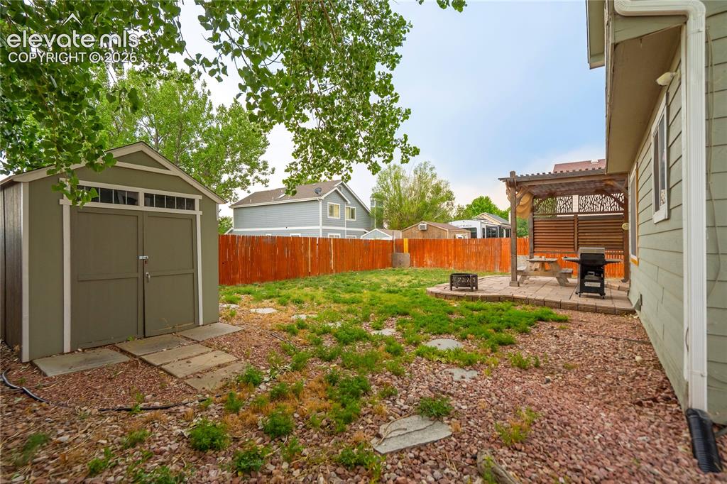 Image 40 of 40: Expansive backyard featuring a shaded patio with pergola, a storage shed wi
