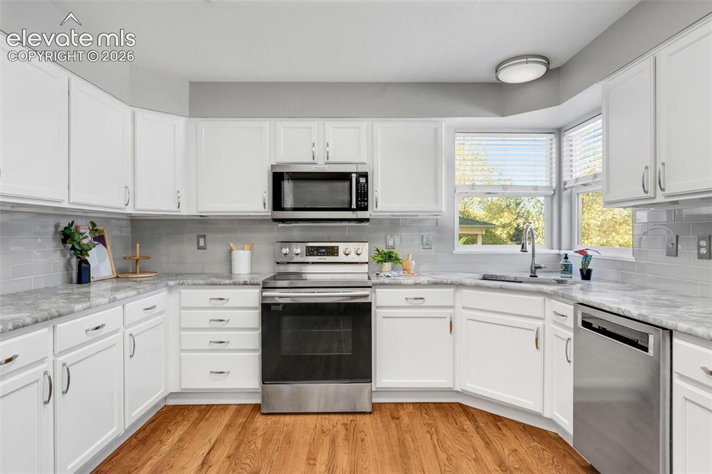 Image 10 of 36: Kitchen featuring white shaker cabinetry, stone-surface countertops, subway