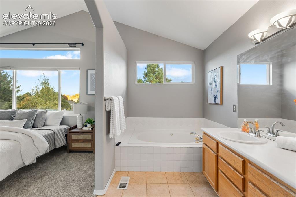 Image 20 of 36: Vaulted ceilings, drop-in soaking tub with white tile surround, vanity with