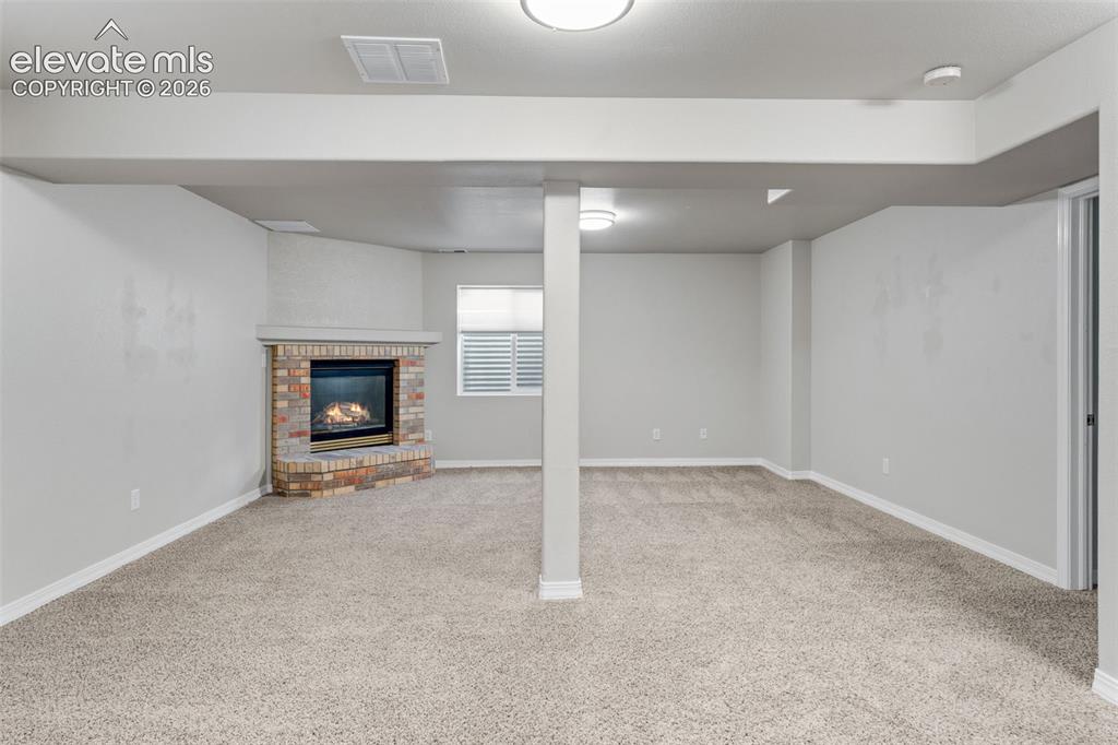 Image 29 of 36: Open-concept area featuring neutral carpeting, a brick-surround corner fire