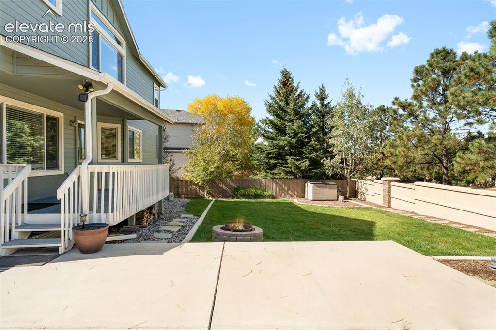 Image 34 of 36: Fenced backyard featuring a raised wooden deck, concrete patio, stone fire 
