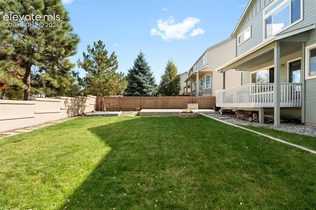 Image 35 of 36: Backyard featuring an elevated wooden deck with railing, a stone-lined fire