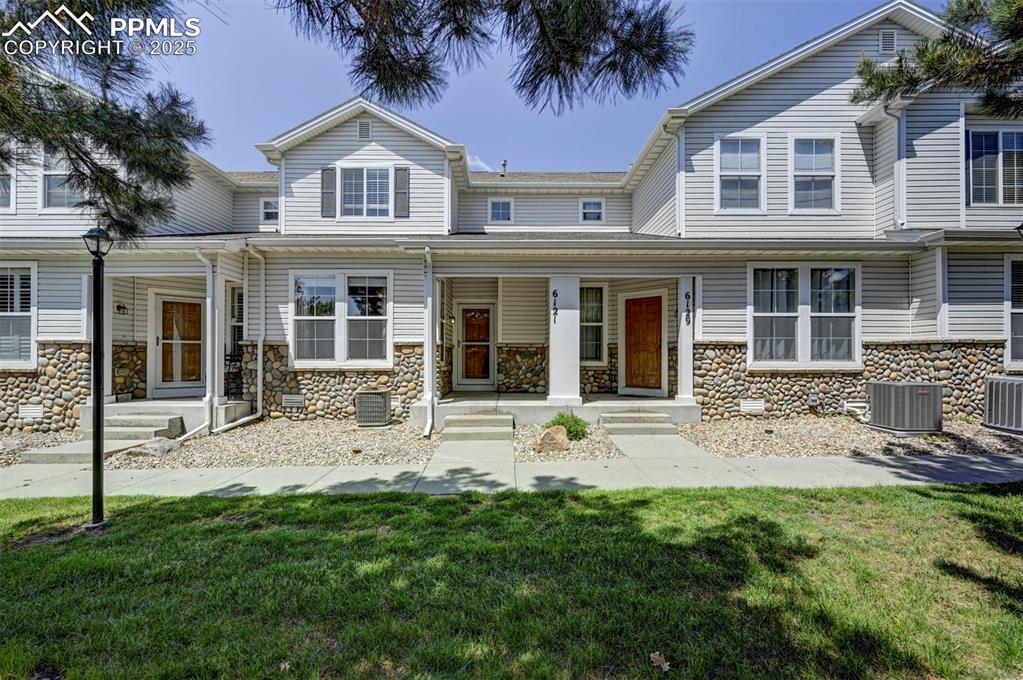 Caption: View of front of house with stone siding, a porch, cooling unit, and a front yard