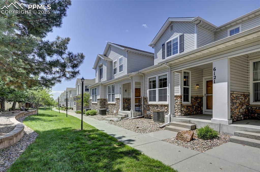 Image 3 of 26: View of side of property with stone siding, a lawn, covered porch, and cent